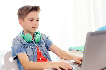 Image showing happy boy with headphones typing on laptop at home