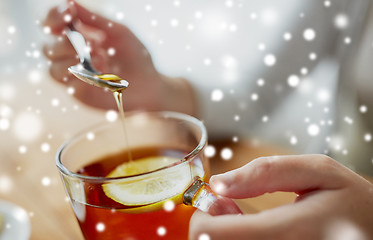 Image showing close up of woman adding honey to tea with lemon