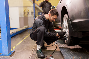 Image showing auto mechanic with screwdriver changing car tire