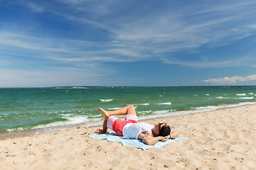 Image showing happy smiling young man sunbathing on beach towel