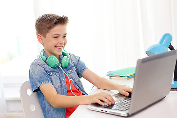 Image showing happy boy with headphones typing on laptop at home