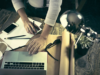 Image showing Vintage hipster wooden desktop top view, male hands using a laptop and holding a pencil