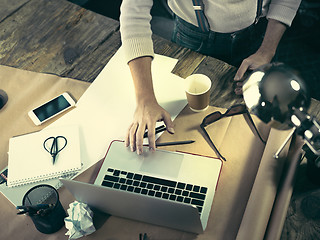 Image showing Vintage hipster wooden desktop top view, male hands using a laptop and holding a pencil