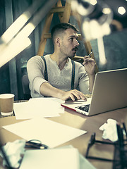 Image showing Portrait of a bearded businessman who is checking details of his upcoming meeting in his notebook and typing.