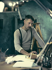 Image showing Portrait of a bearded businessman who is checking details of his upcoming meeting in his notebook and typing.