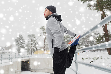 Image showing sports man stretching leg at fence in winter