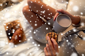 Image showing close up of woman with cocoa cup and cookie in bed