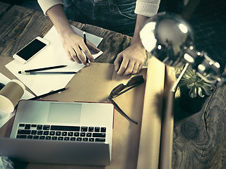 Image showing Vintage hipster wooden desktop top view, male hands using a laptop and holding a pencil