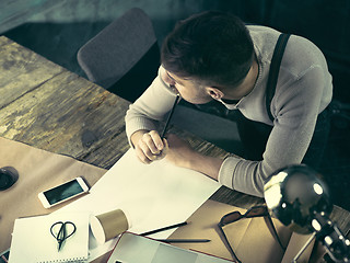 Image showing Vintage hipster wooden desktop top view, male hands using a laptop and holding a pencil