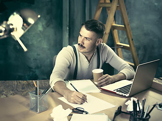 Image showing Portrait of a bearded businessman who is checking details of his upcoming meeting in his notebook and typing.