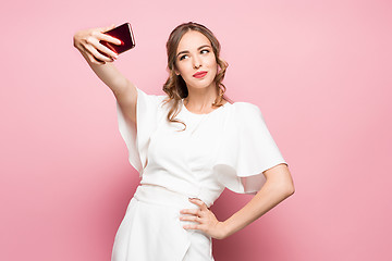 Image showing Portrait of a young attractive woman making selfie photo with smartphone on a pink background