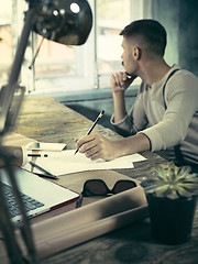 Image showing Portrait of a bearded businessman who is checking details of his upcoming meeting in his notebook and typing.