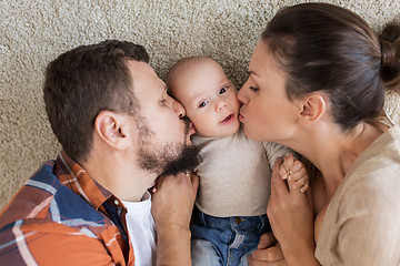 Image showing happy family lying on floor and kissing their baby
