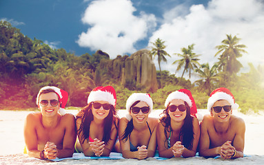 Image showing friends in santa hats on beach at christmas