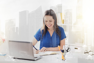 Image showing happy woman writing to notebook at office