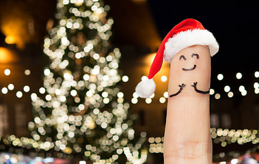 Image showing finger with smiley in santa hat at christmas tree