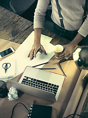 Image showing Vintage hipster wooden desktop top view, male hands using a laptop and holding a pencil