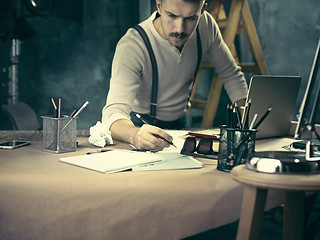 Image showing Portrait of a bearded businessman who is checking details of his upcoming meeting in his notebook and typing.