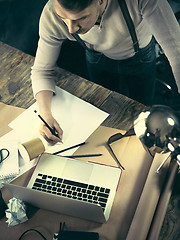 Image showing Vintage hipster wooden desktop top view, male hands using a laptop and holding a pencil