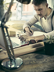 Image showing Portrait of a bearded businessman who is checking details of his upcoming meeting in his notebook and typing.