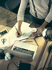 Image showing Vintage hipster wooden desktop top view, male hands using a laptop and holding a pencil