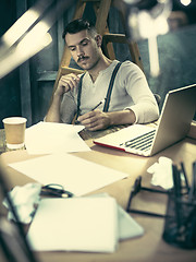 Image showing Portrait of a bearded businessman who is checking details of his upcoming meeting in his notebook and typing.