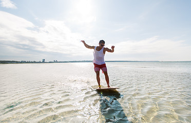 Image showing young man riding on skimboard on summer beach