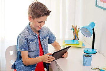 Image showing smiling boy with tablet pc sitting at home desk