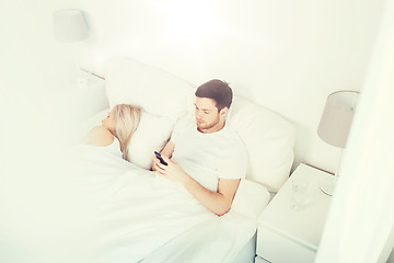 Image showing man texting message while woman is sleeping in bed