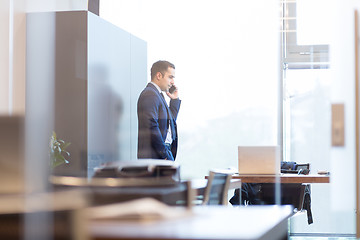 Image showing Businessman talking on a mobile phone while looking through window.