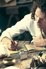 Image showing Writer at work. Handsome young writer sitting at the table and writing something in his sketchpad