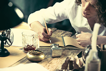 Image showing Writer at work. Handsome young writer sitting at the table and writing something in his sketchpad