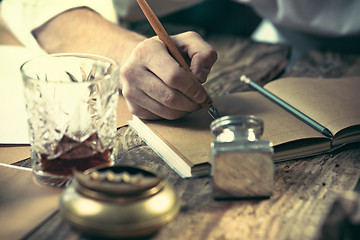 Image showing Writer at work. The hands of young writer sitting at the table and writing something in his sketchpad