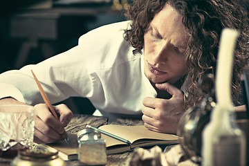 Image showing Writer at work. Handsome young writer sitting at the table and writing something in his sketchpad