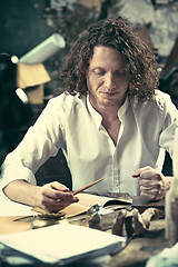 Image showing Writer at work. Handsome young writer sitting at the table and writing something in his sketchpad