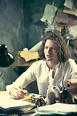 Image showing Writer at work. Handsome young writer sitting at the table and writing something in his sketchpad