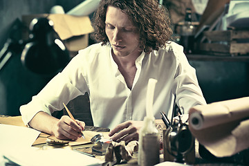 Image showing Writer at work. Handsome young writer sitting at the table and writing something in his sketchpad