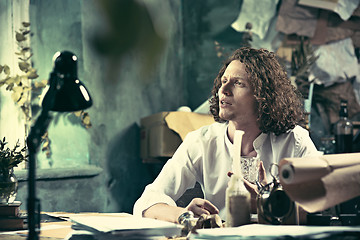 Image showing Writer at work. Handsome young writer sitting at the table and writing something in his sketchpad