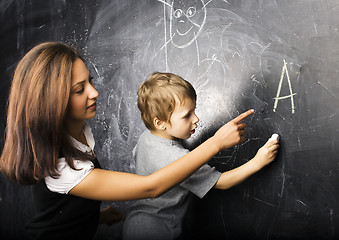 Image showing little cute boy in glasses with young real teacher, classroom studying at blackboard school