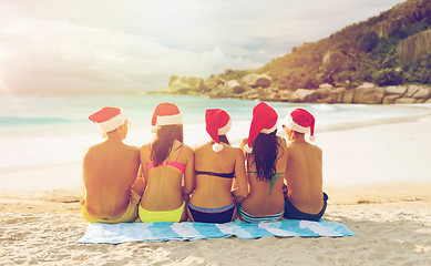 Image showing friends in santa hats on beach at christmas