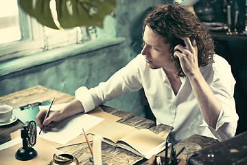 Image showing Writer at work. Handsome young writer sitting at the table and writing something in his sketchpad