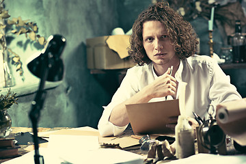 Image showing Writer at work. Handsome young writer sitting at the table and writing something in his sketchpad