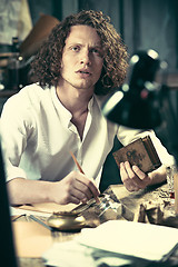 Image showing Writer at work. Handsome young writer sitting at the table and writing something in his sketchpad