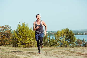 Image showing Running sport. Man runner sprinting outdoor in scenic nature. Fit muscular male athlete training trail running for marathon run.