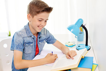 Image showing student boy with book writing to notebook at home