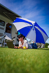 Image showing Woman on the grass, looking at the laptop under umbrella near th