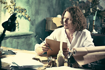 Image showing Writer at work. Handsome young writer sitting at the table and writing something in his sketchpad