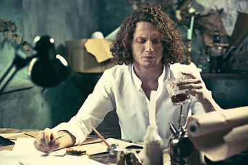 Image showing Writer at work. Handsome young writer sitting at the table and writing something in his sketchpad