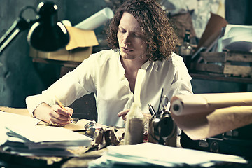 Image showing Writer at work. Handsome young writer sitting at the table and writing something in his sketchpad