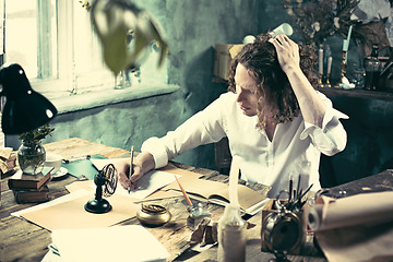 Image showing Writer at work. Handsome young writer sitting at the table and writing something in his sketchpad